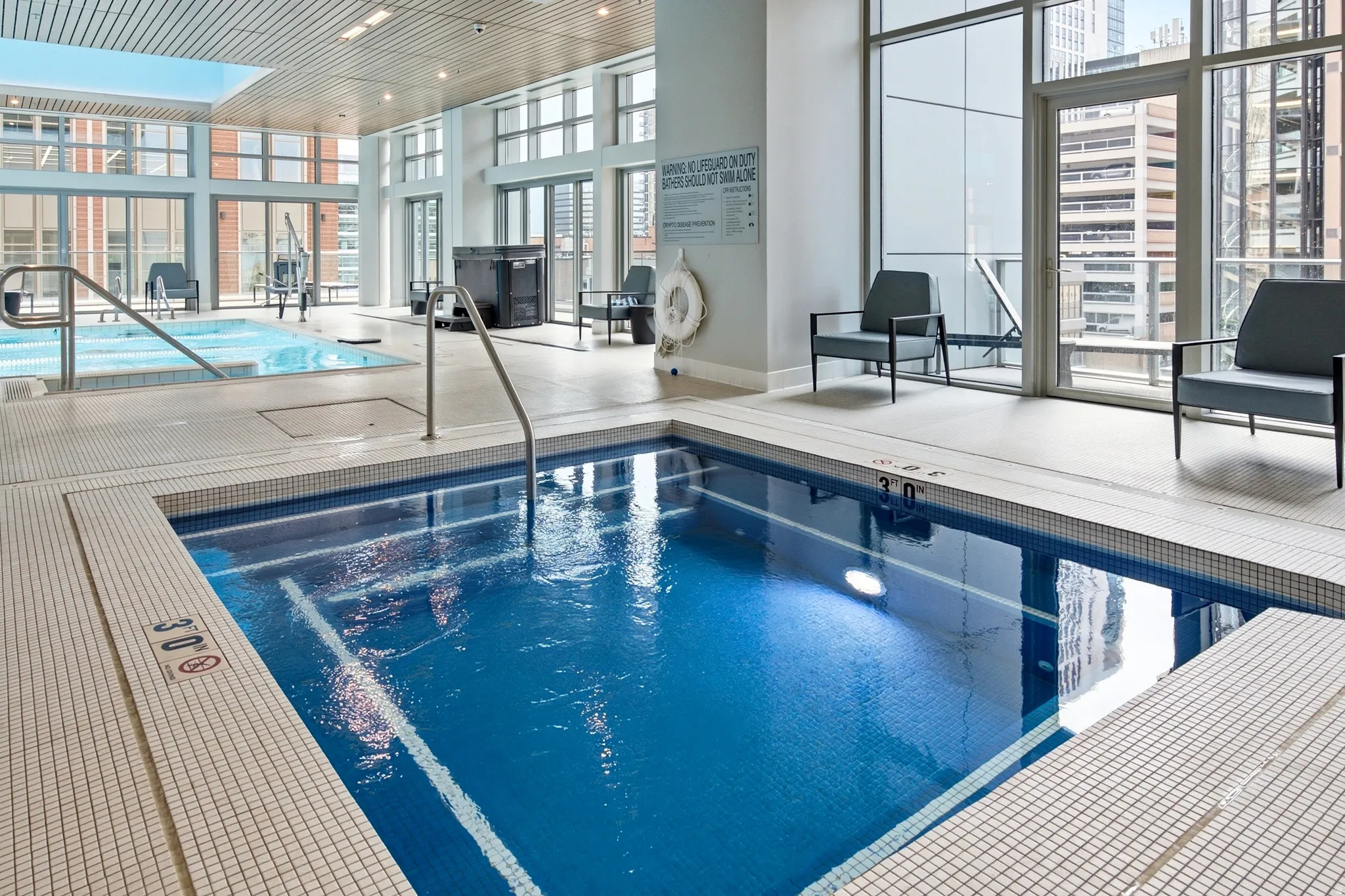 Indoor aquatic area featuring a tiled soaking pool with handrails, a secondary tiled pool, and expansive windows