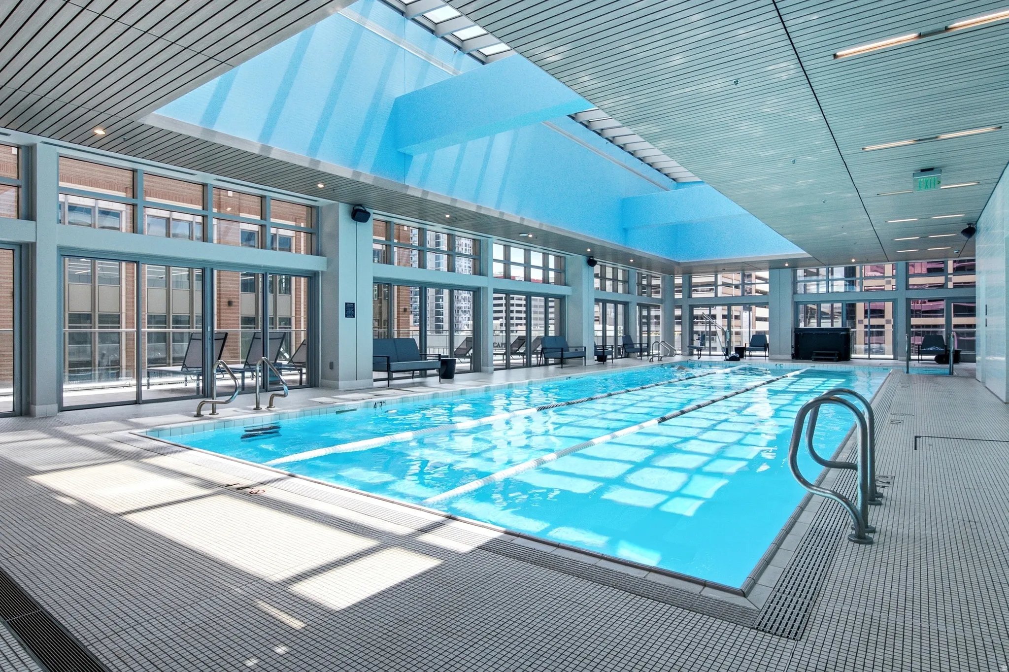Indoor lap pool featuring a large overhead skylight, extensive window walls, recessed ceiling lighting, and a white tile surround