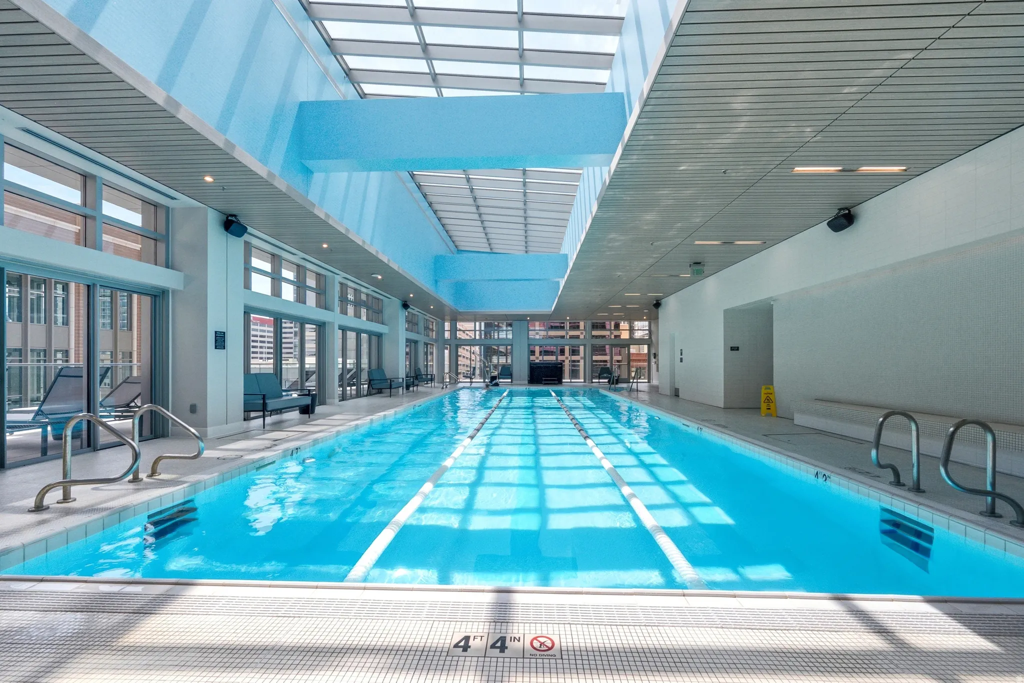 Indoor lap pool featuring a clear skylight ceiling, perimeter windows, and white tiled flooring