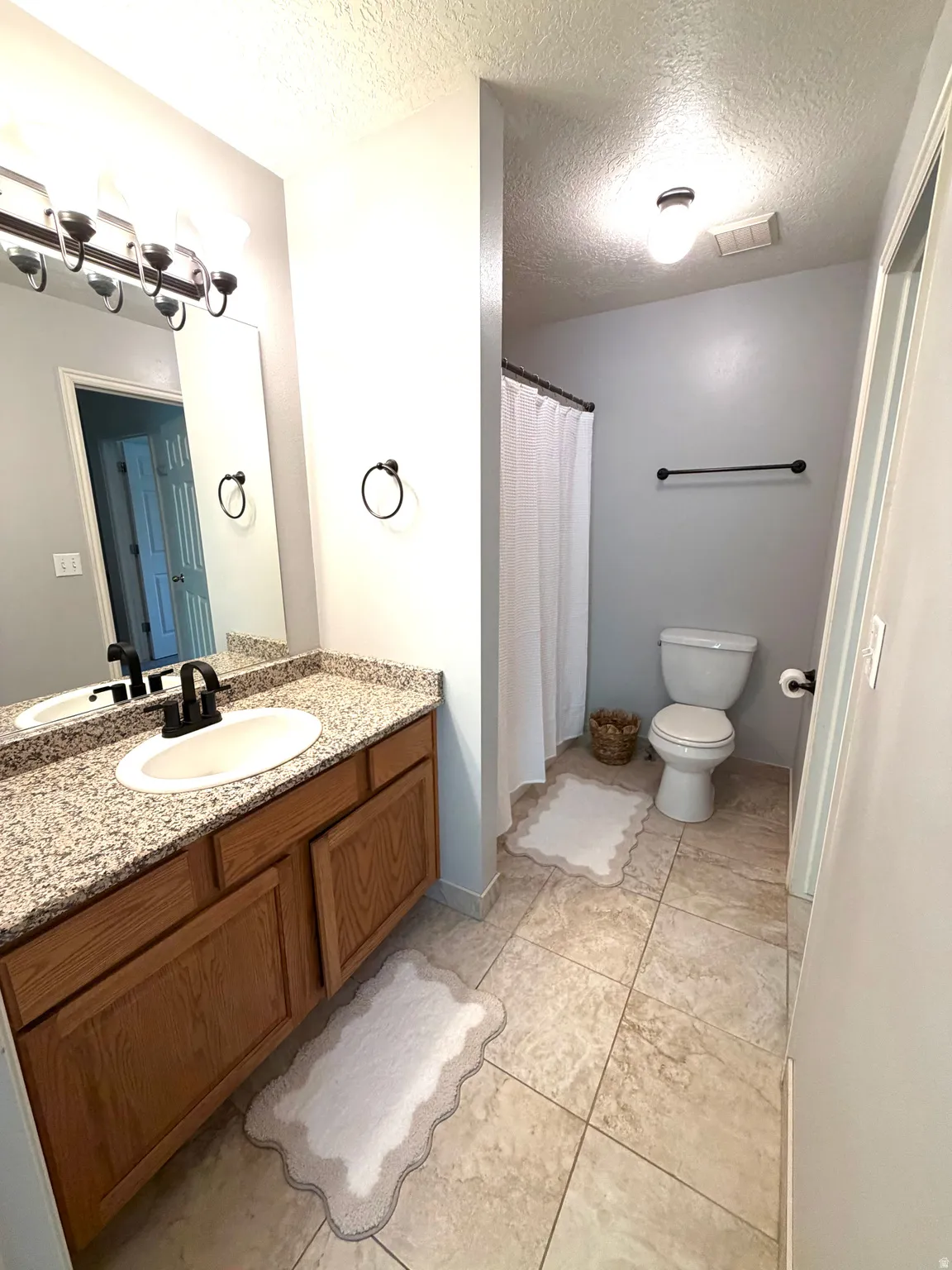 Bathroom featuring a wood-finish vanity with granite countertop, integrated oval sink, and a dark bronze faucet