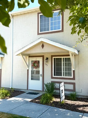 Two-story stucco exterior featuring a covered entry, white window frames with contrasting trim, and a concrete walkway