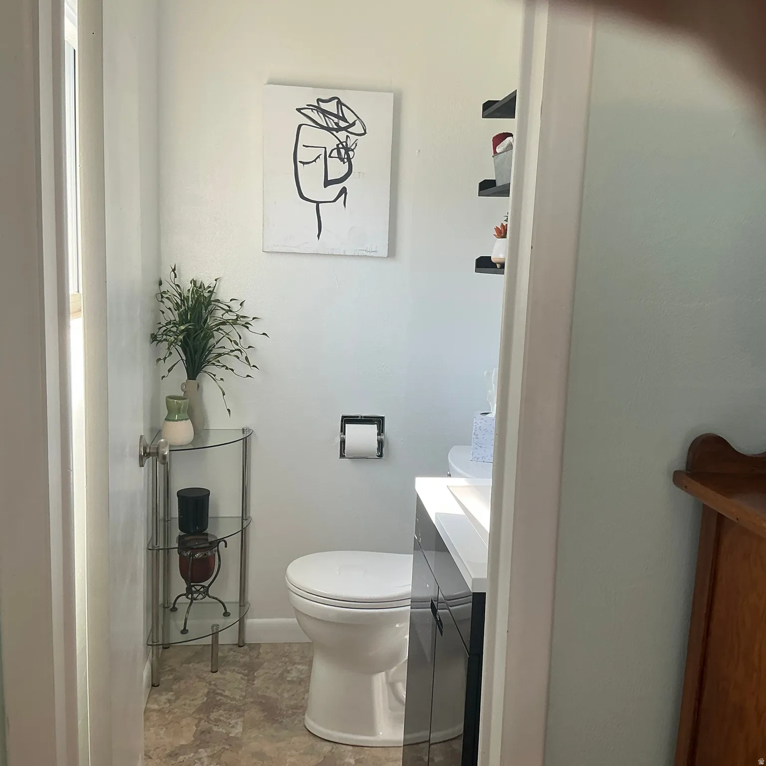 Compact bathroom featuring a white toilet, dark vanity with a white countertop, and light-toned flooring
