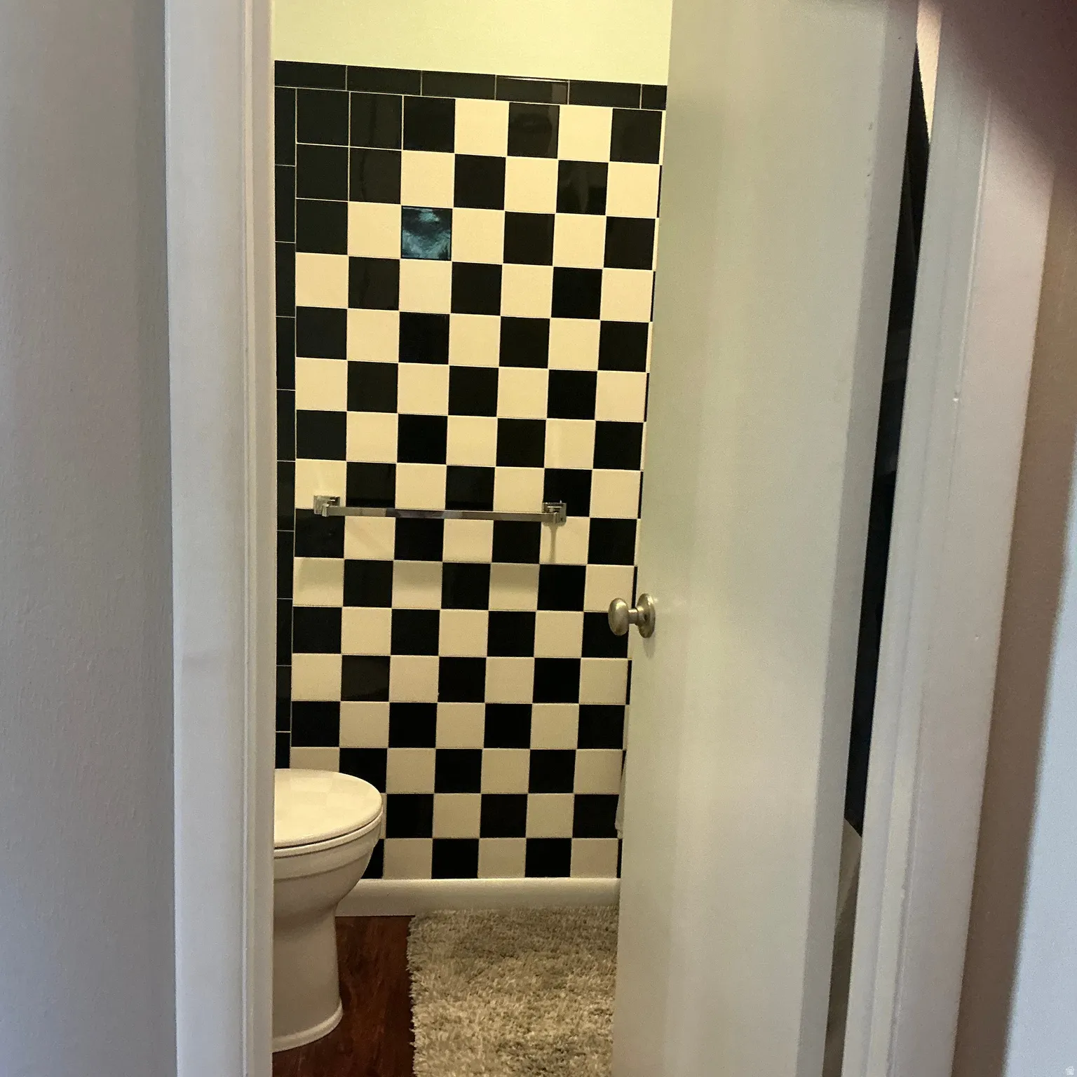 Bathroom featuring checkerboard wall tiling, a white toilet, and wood-finish flooring