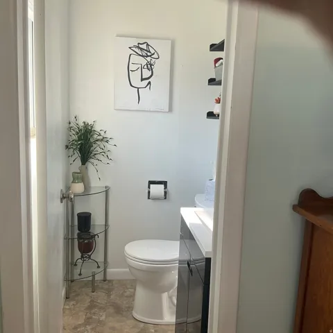Compact bathroom featuring a white toilet, dark vanity with a white countertop, and light-toned flooring