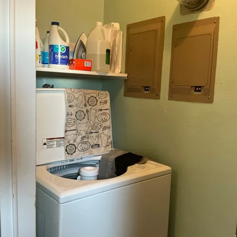 Dedicated laundry area featuring a white top-load washing machine, an overhead shelf, and two wall-mounted utility panels