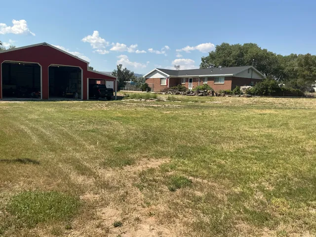 Expansive lot featuring a red barn with open bays and a brick residence with a dark roof and mature trees