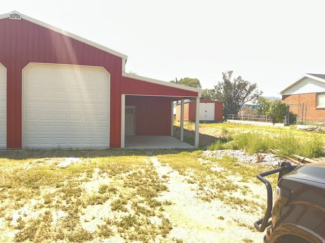 Red metal-sided structure featuring multiple large roll-up doors, a covered concrete pad, and an entry door