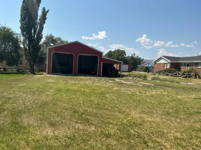 Two-bay red barn structure with an extended side awning, situated on a grassy lot