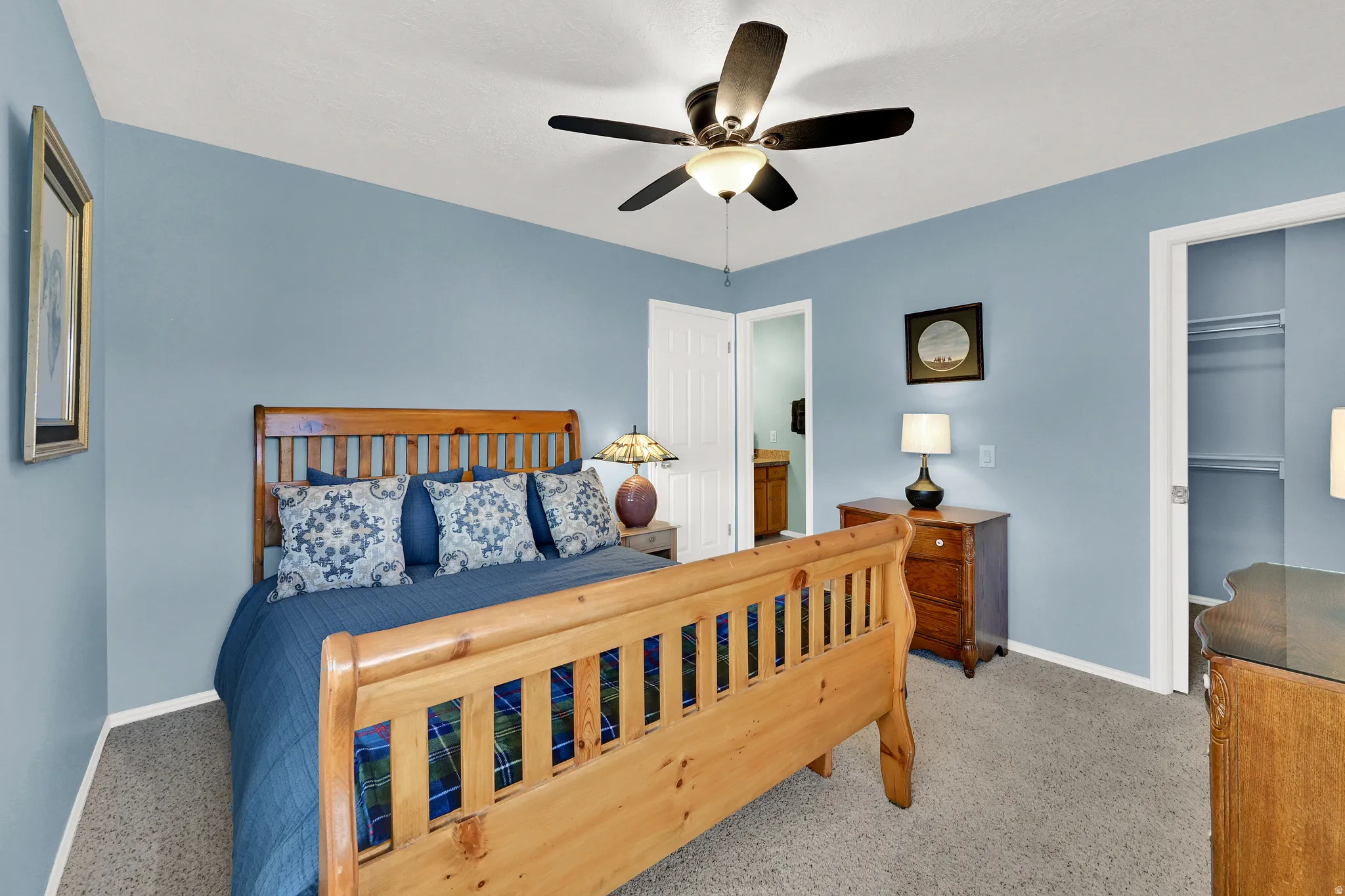 Carpeted bedroom featuring light blue walls, a ceiling fan with integrated lighting, a wooden door, and a built-in closet with shelving