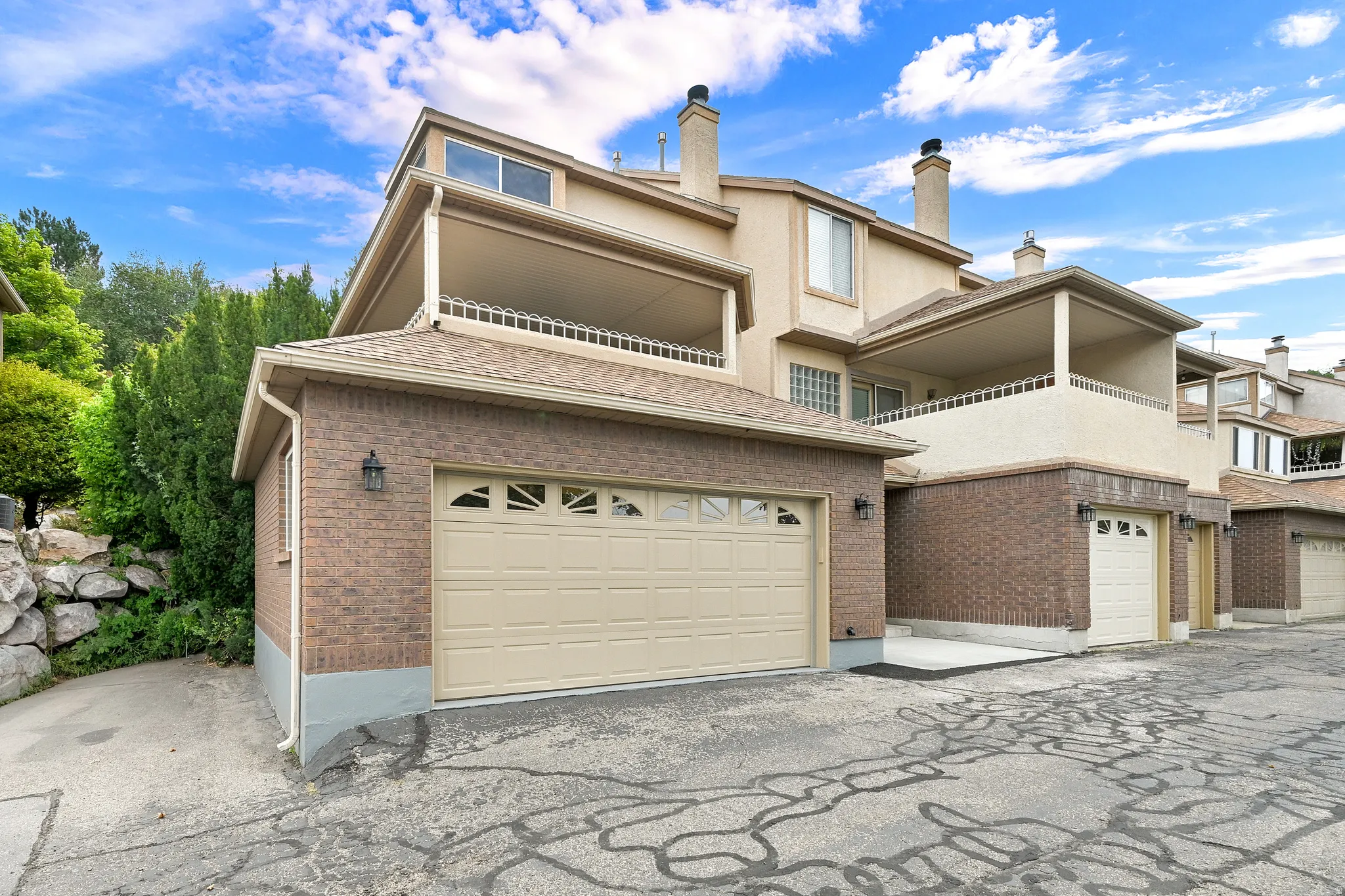 Multi-level property exterior featuring a two-car garage, brick facade, and an upper-level covered balcony