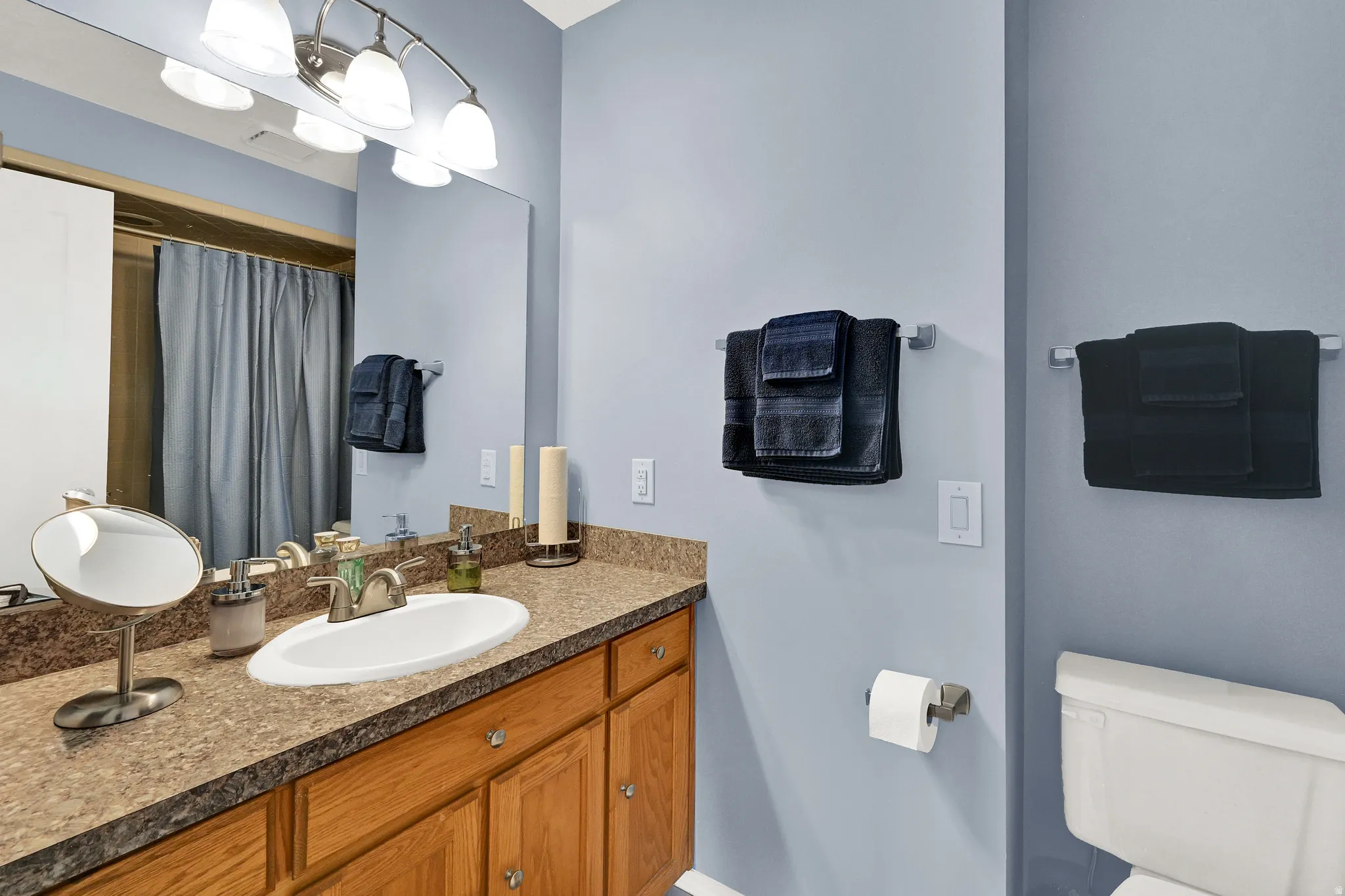 Single vanity featuring a solid surface countertop, an undermount sink with a brushed nickel faucet, and wood-finish cabinetry
