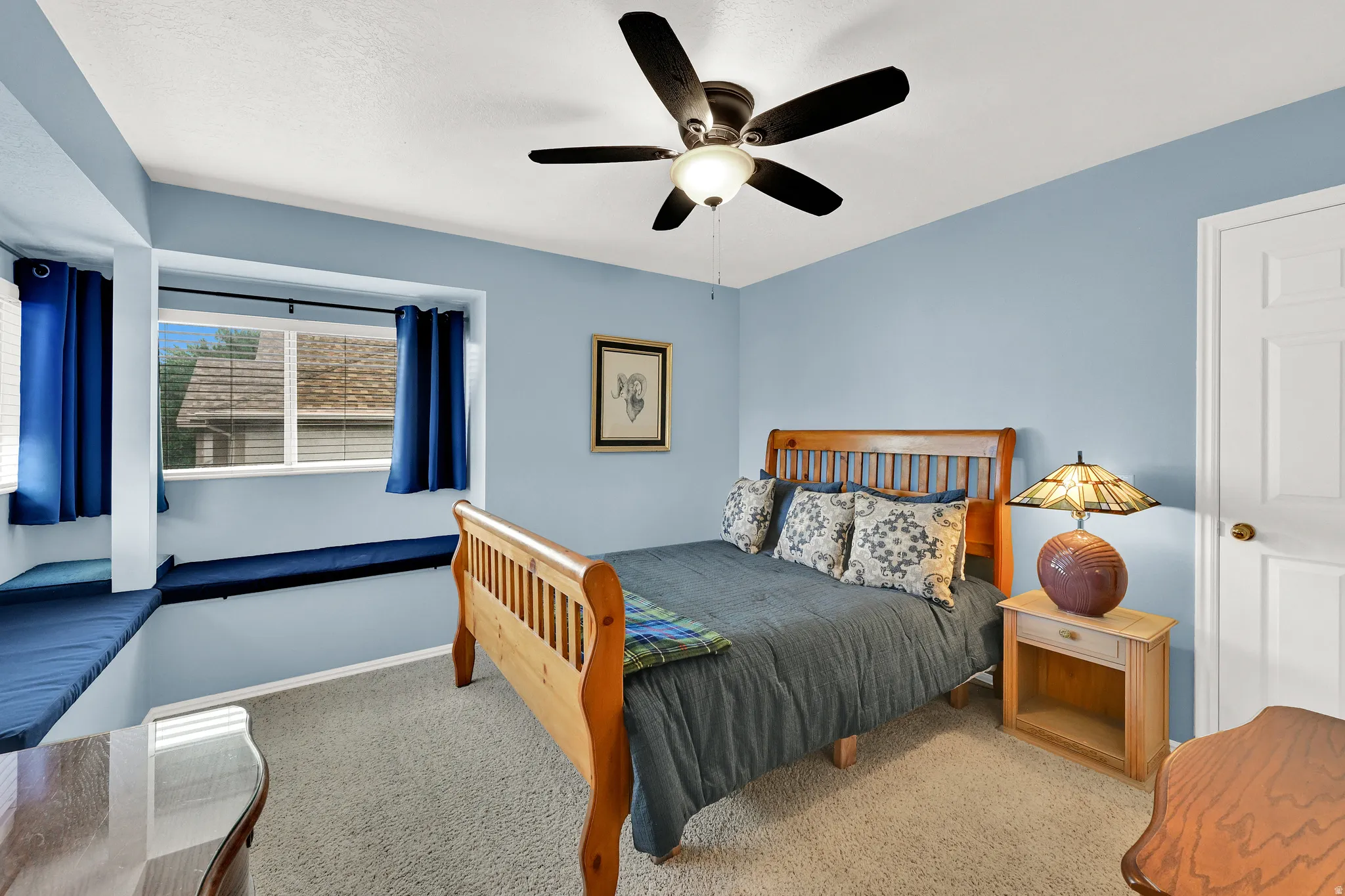 Carpeted room featuring a built-in window bench with blue cushions, a ceiling fan with integrated lighting, and light blue wall paint
