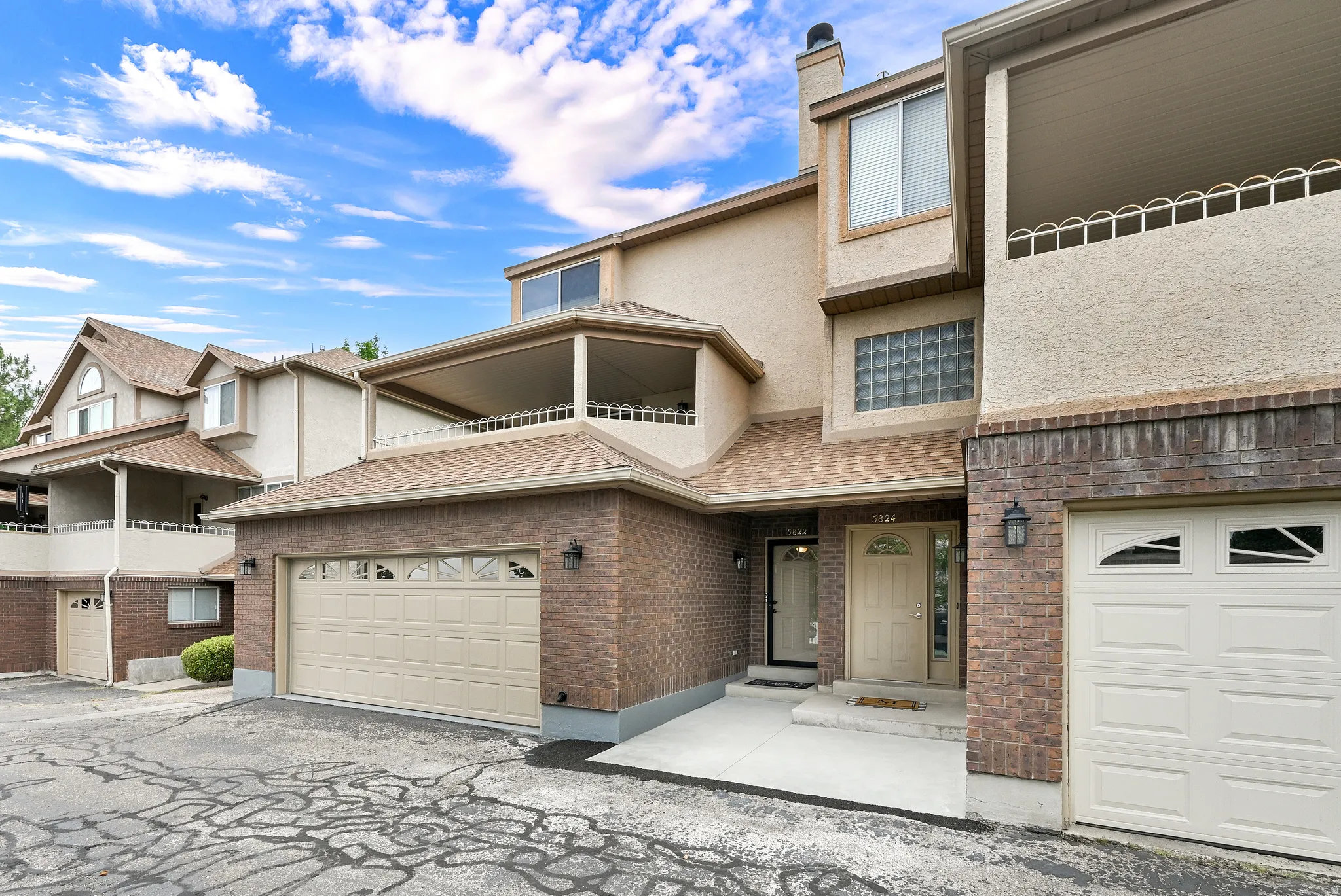Multi-level exterior featuring a brick and stucco facade, a two-car garage, an enclosed porch with balustrade, and a prominent glass block window array