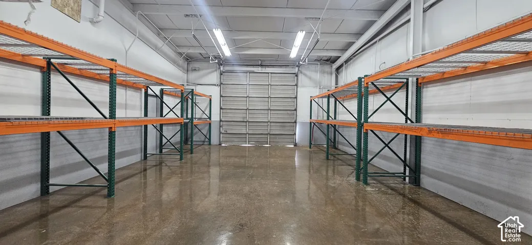 Warehouse space featuring concrete flooring, overhead fluorescent lighting, a large roll-up door, and extensive industrial shelving
