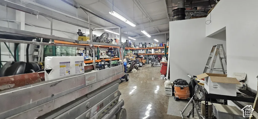 Spacious industrial interior featuring high ceilings, fluorescent lighting, polished concrete flooring, exposed overhead ductwork, and white painted walls