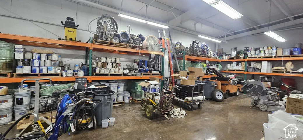 Warehouse interior featuring high ceilings with fluorescent lighting, concrete flooring, and extensive industrial-grade shelving units