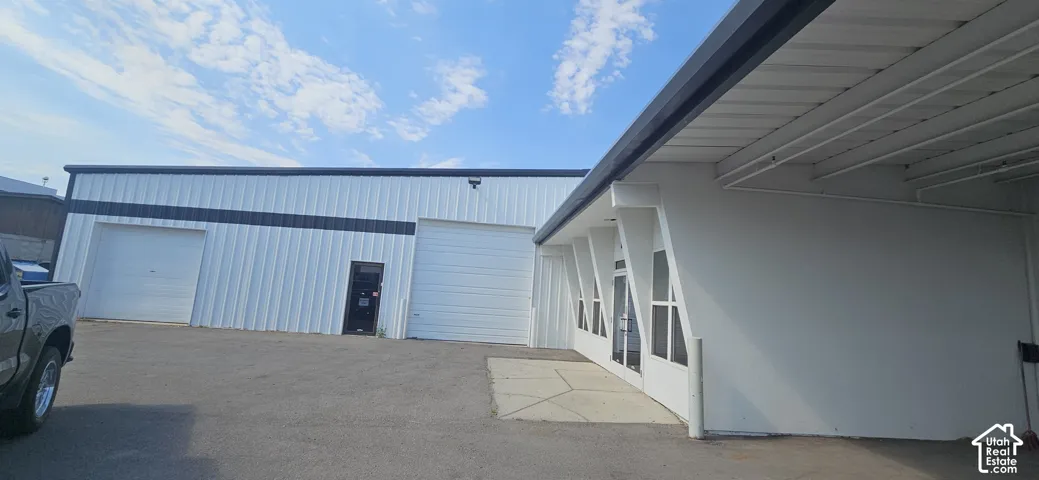 Industrial building with a white corrugated metal exterior, black trim accents, two large overhead doors, a pedestrian entrance, and an attached white stucco-finished structure with multiple windows