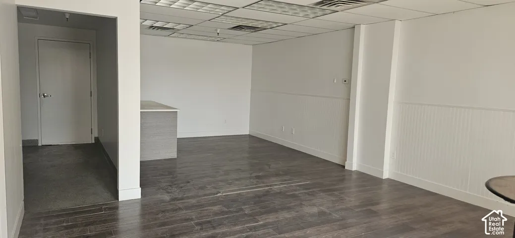 Spacious interior featuring dark wood-finish flooring, white walls, and a dropped acoustic panel ceiling with recessed lighting