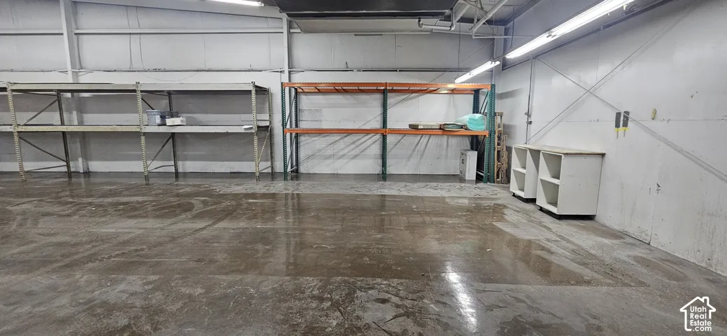 Spacious industrial interior featuring polished concrete flooring, exposed metal structural beams, fluorescent strip lighting, and white wall panels