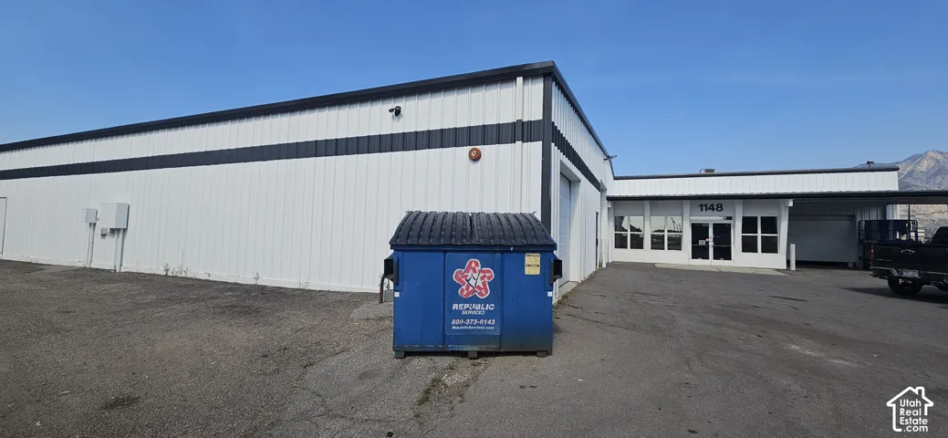 Commercial building featuring white metal siding with dark accent banding, a flat roofline, and multiple access points including a roll-up door and a double-door entrance