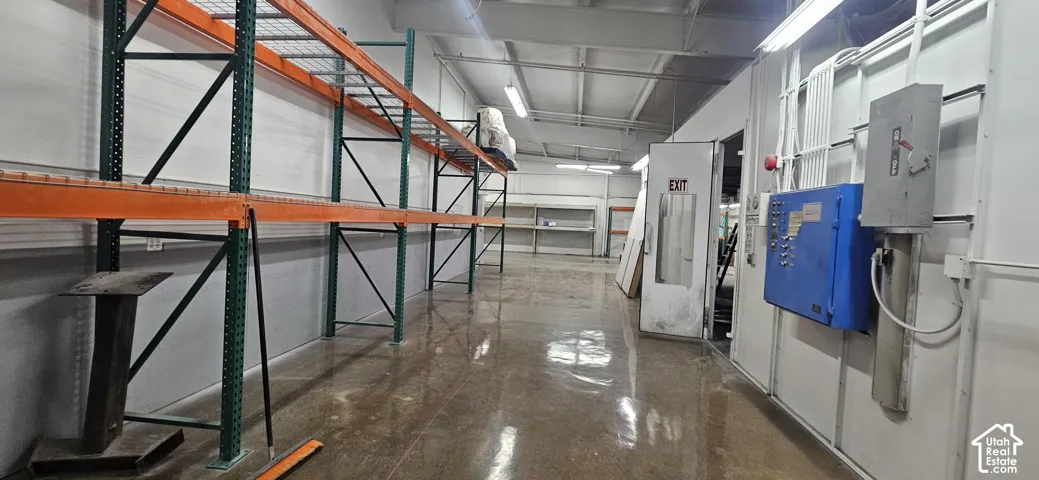 Industrial space featuring high ceilings, polished concrete flooring, extensive pallet racking, fluorescent lighting, and a utility panel