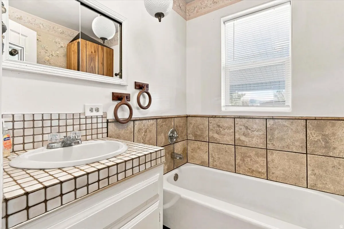 Bathroom featuring a white bathtub, ceramic tile wainscoting, and a single vanity with a tiled countertop and integrated sink