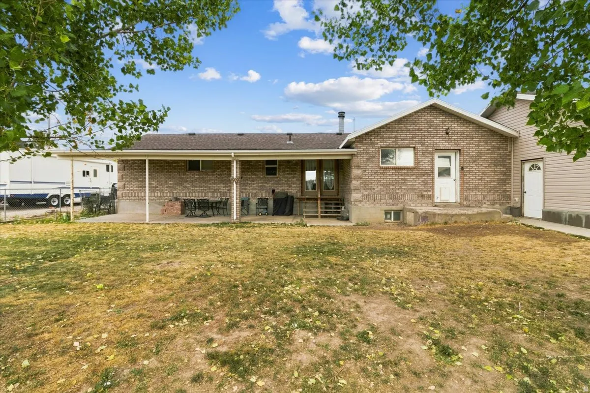 Brick exterior featuring a covered patio with concrete flooring, multiple exterior doors, and a partial view of an outbuilding with siding