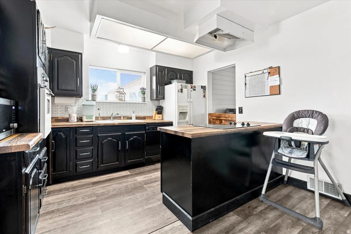 Kitchen featuring black cabinetry, wood-finish countertops, and a full tile backsplash
