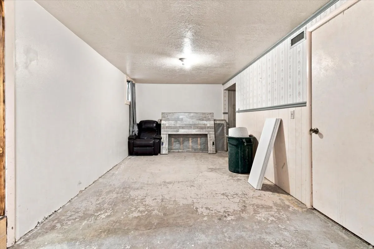 Spacious lower-level room featuring a fireplace with a wood mantel, exposed concrete flooring, and built-in wall paneling