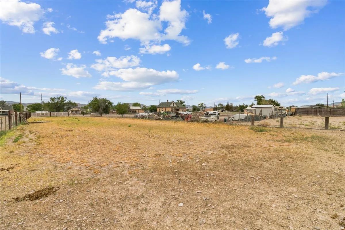 Expansive open lot featuring a perimeter fence and mature trees in the background
