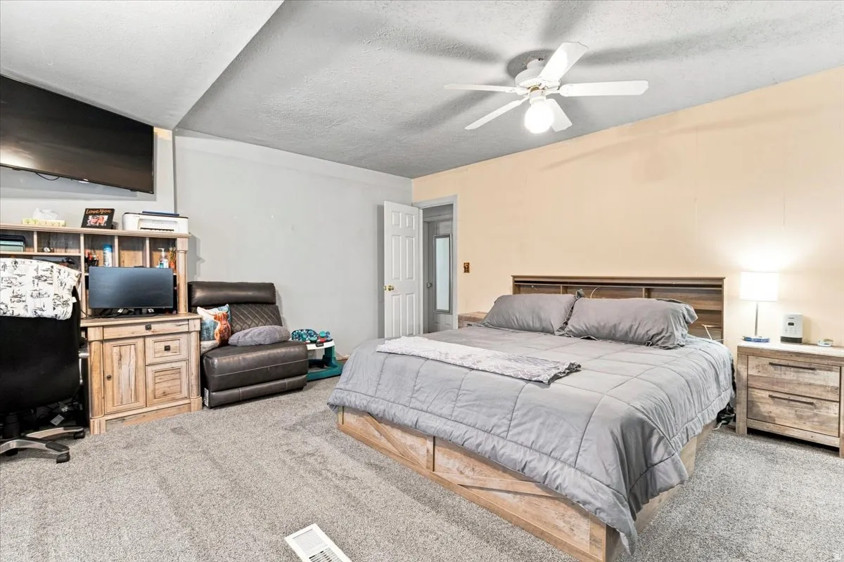 Bedroom featuring neutral-toned walls, textured carpeting, and a ceiling fan with integrated lighting