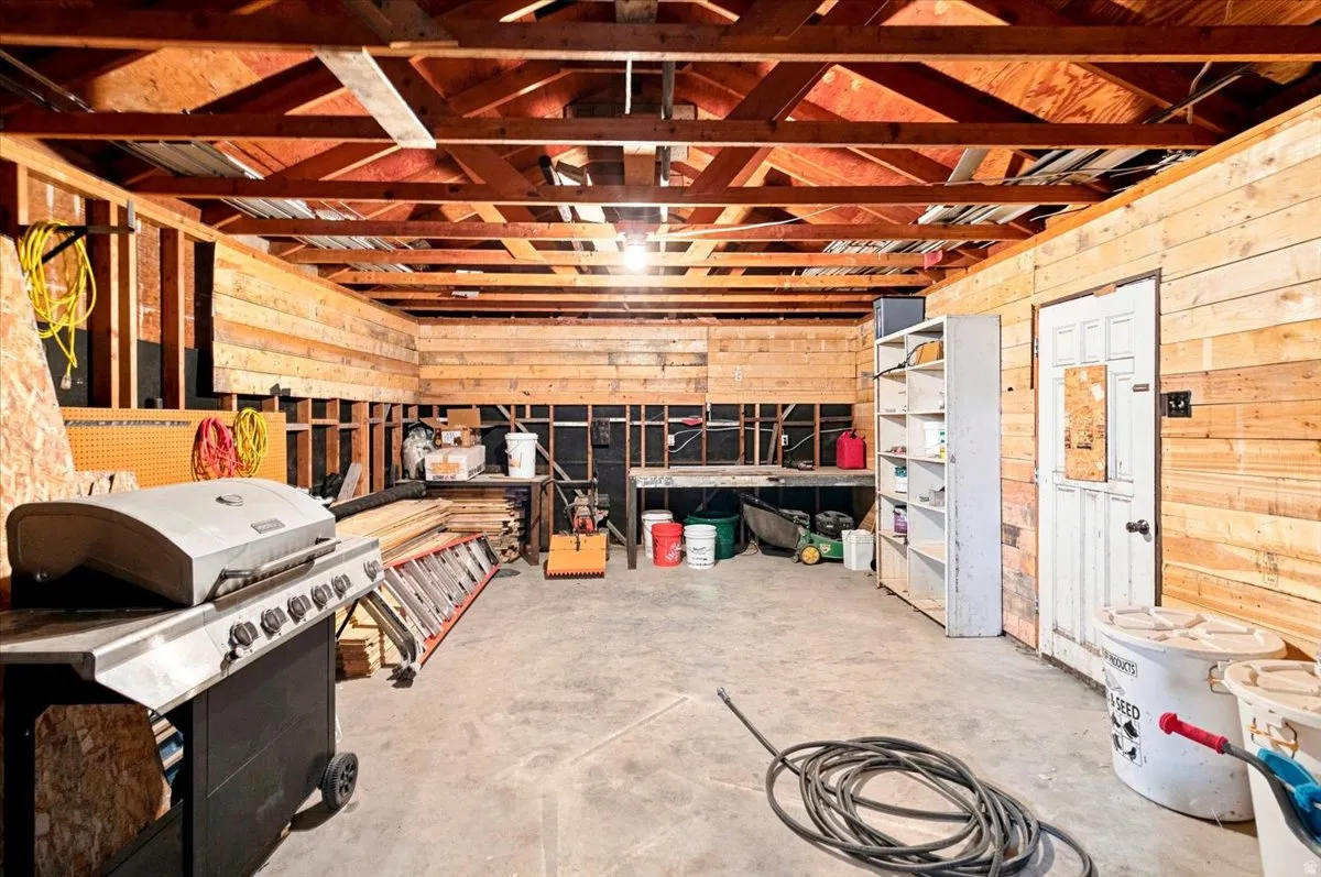 Spacious garage with exposed wood beam ceiling, concrete flooring, and unfinished wood paneling