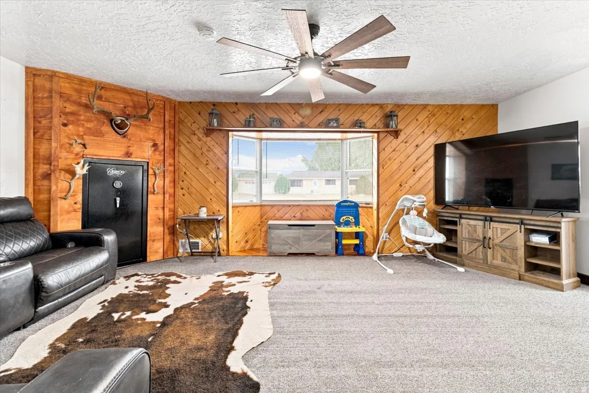 Living area featuring wood paneling, a bay window with a built-in shelf, and a ceiling fan with integrated lighting