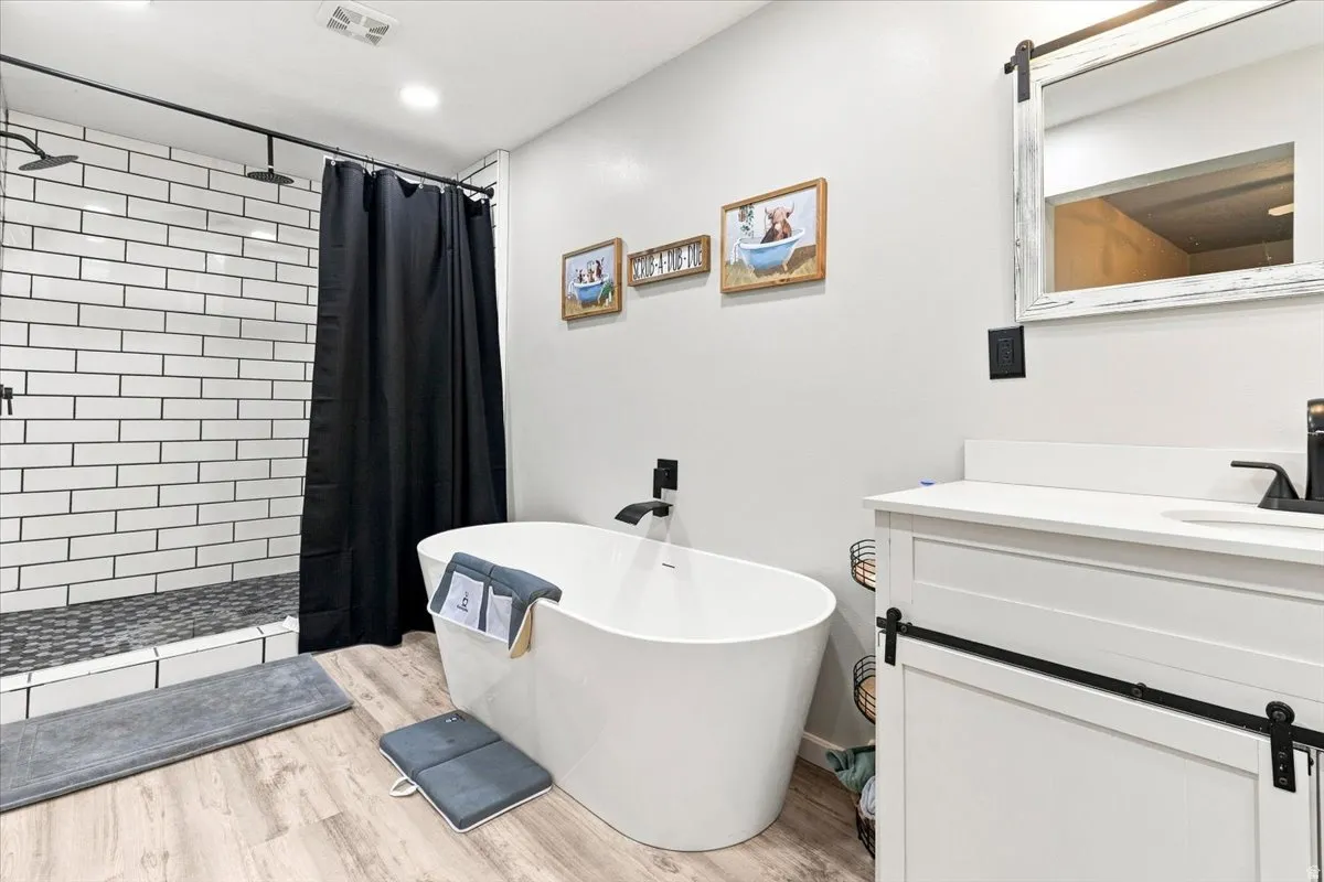 Contemporary bathroom featuring a freestanding soaking tub with a matte black floor-mounted faucet, a walk-in shower with white subway tile and dark grout, and a single vanity with a white countertop and barn door style cabinetry