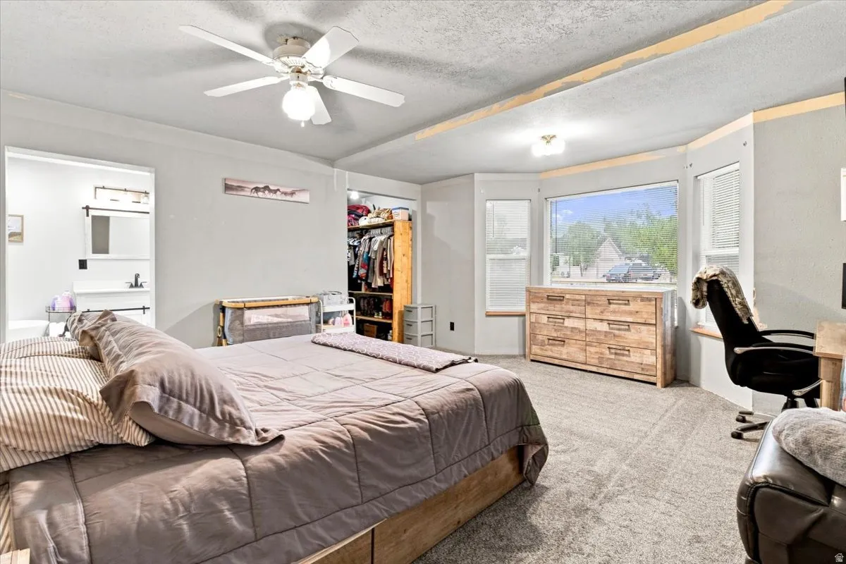 Carpeted room featuring a ceiling fan with integrated lighting, a bay window with a window seat, and an open closet