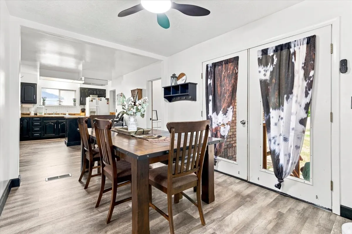 Open-concept dining area featuring wood-finish flooring, a ceiling fan, and French doors