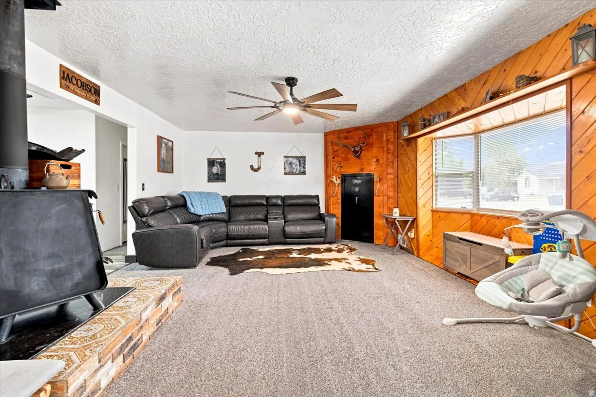 Spacious living area featuring a wood-burning stove with a brick and tile hearth, a ceiling fan, and a large bay window