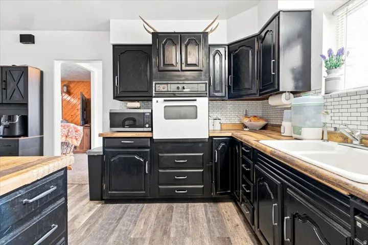 Kitchen featuring black cabinetry, wood-finish countertops, white subway tile backsplash, a built-in wall oven, and wood-finish flooring