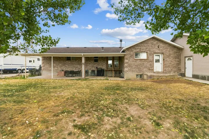 Brick exterior featuring a covered patio with concrete flooring, multiple exterior doors, and a partial view of an outbuilding with siding