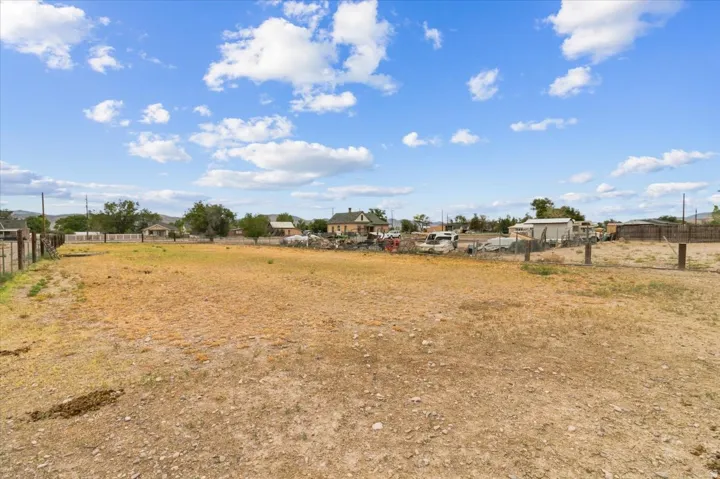 Expansive open lot featuring a perimeter fence and mature trees in the background