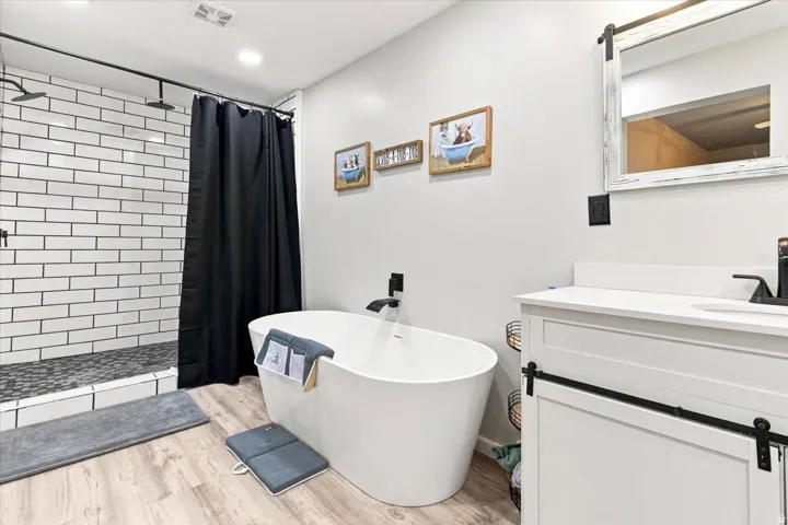 Contemporary bathroom featuring a freestanding soaking tub with a matte black floor-mounted faucet, a walk-in shower with white subway tile and dark grout, and a single vanity with a white countertop and barn door style cabinetry