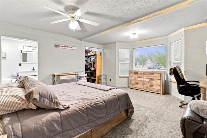Carpeted room featuring a ceiling fan with integrated lighting, a bay window with a window seat, and an open closet