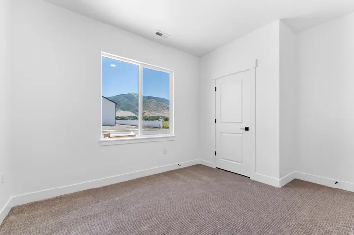 Spacious room featuring a large window with mountain scenery, neutral-toned carpeting, white trim, and a contemporary white panel door with black hardware
