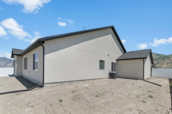 Exterior featuring stucco siding, dark roofing, white frame windows, black gutters, and a sliding glass door