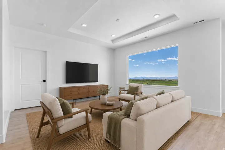 Recessed ceiling lighting, tray ceiling detail, large picture window with outdoor scenery, wood-finish flooring, and white interior doors with dark hardware