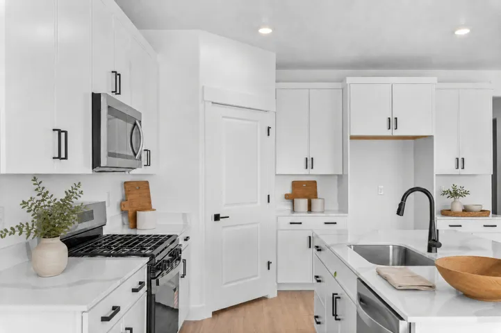 Bright kitchen featuring white cabinetry, stainless steel appliances, a center island with sink, and wood-finish flooring