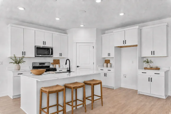 Kitchen featuring white cabinetry with black hardware, stainless steel microwave, light wood-finish flooring, and a central island with a sink and seating