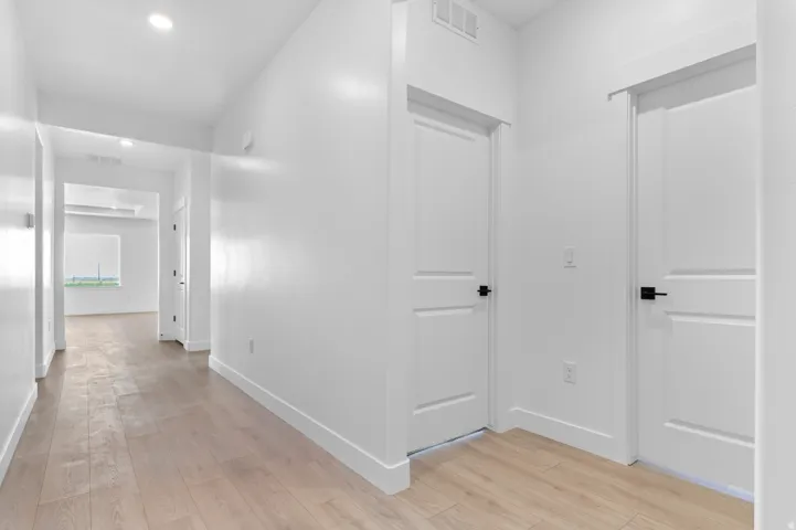 Hallway featuring light wood-finish flooring, white walls, recessed ceiling lighting, and multiple paneled doors with matte black hardware