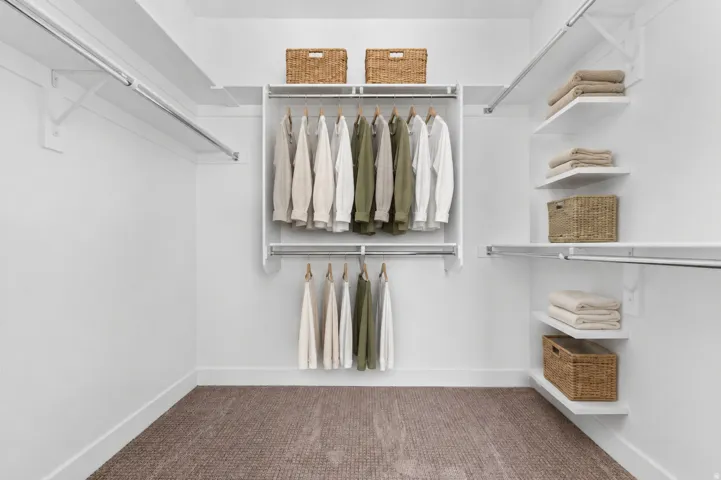 White custom closet system featuring multiple hanging rods, integrated shelving, and a neutral-toned carpet