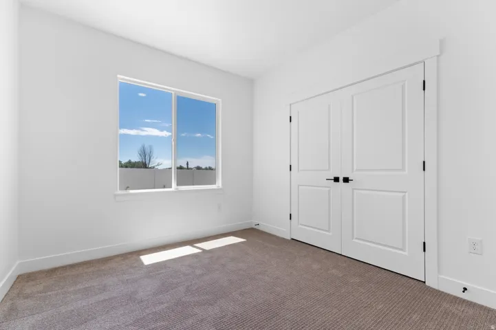 Bright room featuring a large window, neutral carpeting, white walls, and a double-door closet with matte black hardware